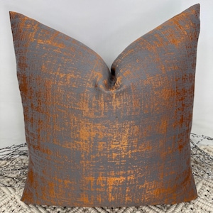 May include: A grey and copper throw pillow with a textured, distressed look. The pillow is made of a soft, comfortable fabric and is perfect for adding a touch of style to any room.