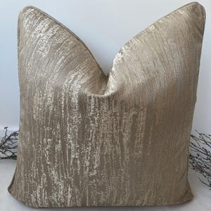 Puede incluir: Una almohada de tiro de color beige y dorado con un patrón texturizado de veta de madera.
