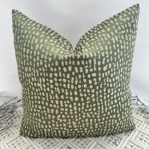 May include: A green cushion with a beige speckled pattern. The cushion is sitting on a white crocheted rug.