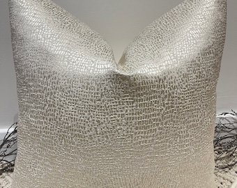 May include: A soft, cream-colored throw pillow with a subtle textured pattern. The pillow is made of a luxurious fabric with a slight sheen.