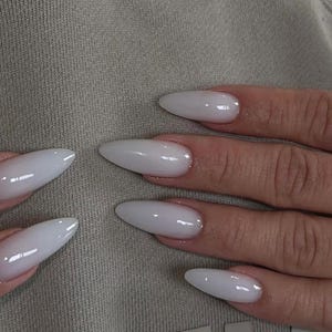 Könnte beinhalten: Nahaufnahme von langen, mandelförmigen Nägeln mit glänzendem weißen Lack.