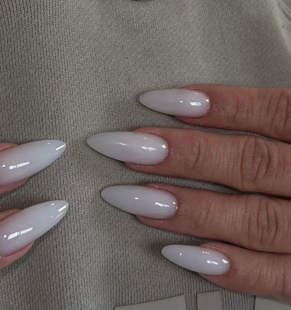 A hand wearing long milky-white almond press-on nails with a glossy finish