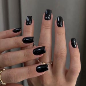 May include: Close-up of hands with short, square-shaped nails painted black.