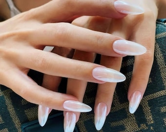 May include: Close-up of a hand with long, oval-shaped nails painted with a sheer white polish. The nails have a subtle shimmer and are slightly iridescent.