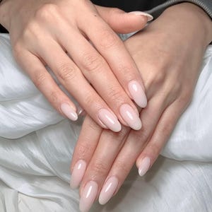 Könnte beinhalten: Zwei Hände mit langen, oval geformten Fingernägeln, die mit einem glänzenden, transparenten hellrosa Nagellack lackiert sind. Die Nägel haben ein glattes, reflektierendes Finish und eine saubere, abgerundete Spitze für ein natürliches Aussehen.