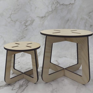 May include: Two wooden stools of different sizes. The stools have a natural wood finish with dark brown edges. Each stool has a round top with four evenly spaced slots and a geometric base with curved legs.