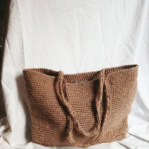 May include: A large, brown, knitted tote bag made of natural fibers. The bag has two long handles and a simple, rustic design.
