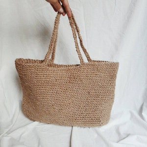 May include: A large, brown, crocheted tote bag made of natural jute fiber. The bag has two thick, woven handles.