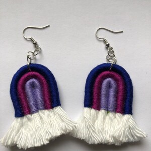May include: A pair of rainbow-colored crocheted earrings with white fringe. The earrings are made with blue, purple, and pink yarn.