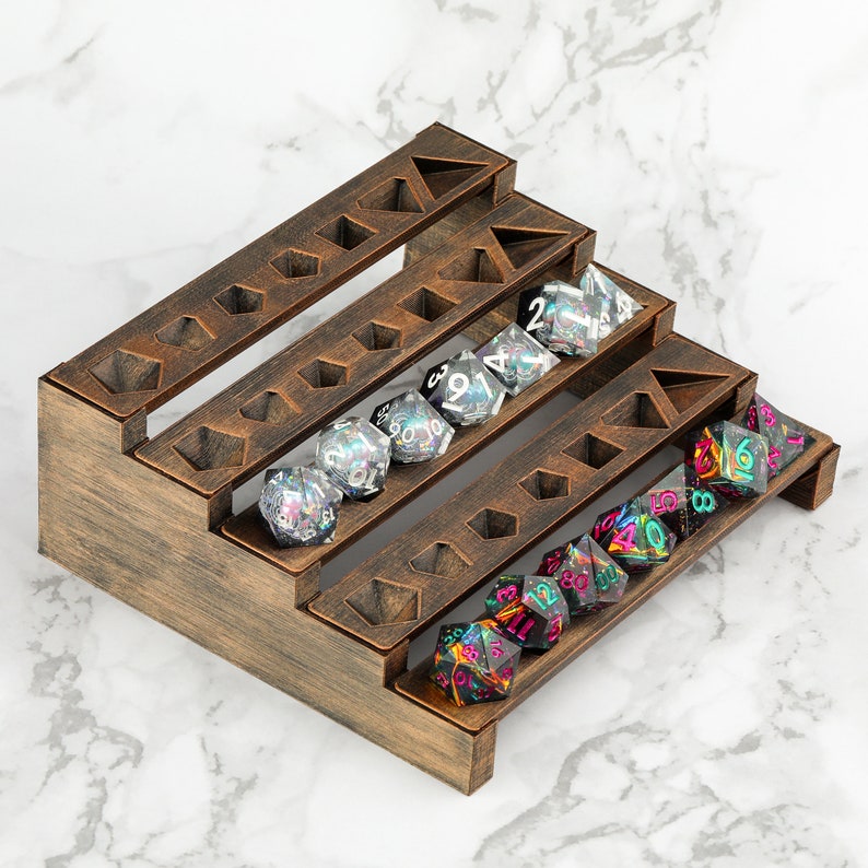 Peut inclure: Un pr&eacute;sentoir &agrave; d&eacute;s en bois &agrave; trois niveaux, teint&eacute; brun fonc&eacute;. Il contient plusieurs d&eacute;s multi-faces de diff&eacute;rentes couleurs, dont transparent, rose et vert. Le pr&eacute;sentoir comporte des d&eacute;coupes g&eacute;om&eacute;triques.