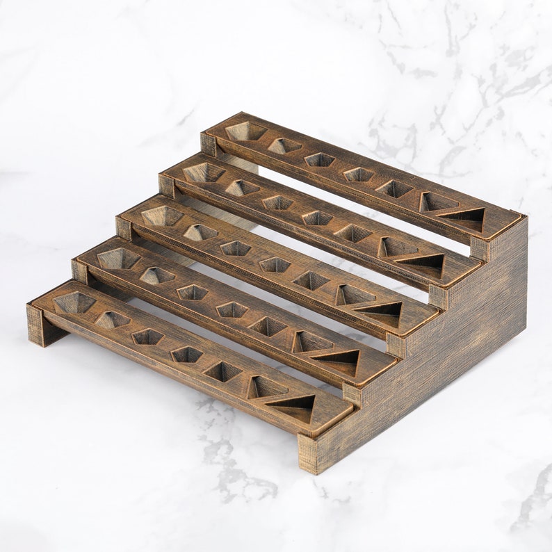 Peut inclure: Un pr&eacute;sentoir en bois &agrave; quatre niveaux en escalier. Chaque niveau comporte plusieurs d&eacute;coupes g&eacute;om&eacute;triques, dont des hexagones et des triangles, con&ccedil;ues pour contenir de petits objets. Le pr&eacute;sentoir a une finition marron fonc&eacute; et est pos&eacute; sur un fond en marbre blanc.