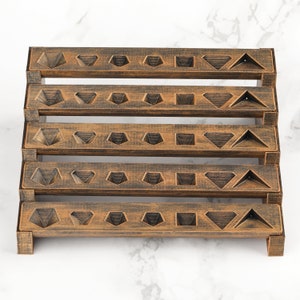 Peut inclure: Pr&eacute;sentoir en bois &agrave; plusieurs niveaux avec une finition bronze vieilli. Chaque niveau pr&eacute;sente des d&eacute;coupes g&eacute;om&eacute;triques en forme de diamants, triangles et carr&eacute;s. Le pr&eacute;sentoir est con&ccedil;u pour contenir de petits objets, tels que des bijoux ou des objets de collection.