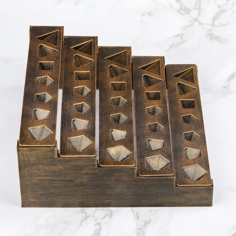 Peut inclure: Un organiseur de bureau en bois brun fonc&eacute; avec un design en escalier. Il pr&eacute;sente des d&eacute;coupes g&eacute;om&eacute;triques de diff&eacute;rentes formes, dispos&eacute;es en colonnes verticales. L'organisateur est con&ccedil;u pour ranger des articles de papeterie ou de petits objets.