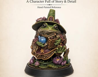 Op de afbeelding: Een handbeschilderd kikker-fantasie-miniatuur met een groene kikker in een puntmuts en een donkerpaarse mantel met gouden sterren. De kikker houdt een blauw flesje en een boek vast en staat op een voetstuk versierd met paarse lotusbloemen.