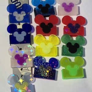 Peut inclure: Une collection d'accessoires en résine colorée en forme de Mickey Mouse. Les accessoires présentent diverses couleurs, dont le bleu, le rouge, le jaune et le vert, avec des visages de souris noirs. Certains ont des paillettes et des étoiles. Pour l'artisanat ou les bijoux.