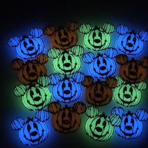 May include: A collection of Halloween-themed decorations featuring pumpkin-shaped designs with Mickey Mouse ears. The pumpkins glow in shades of orange, green, and blue against a dark background. Each pumpkin has a smiling face.