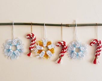 May include: Five handmade Christmas ornaments hanging from a wooden dowel. The ornaments are made of white and red yarn and are shaped like snowflakes and candy canes.