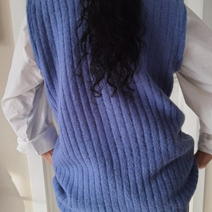Puede incluir: Un chaleco de punto azul sin mangas con textura de canal&eacute;. El chaleco se lleva sobre una camisa blanca abotonada.