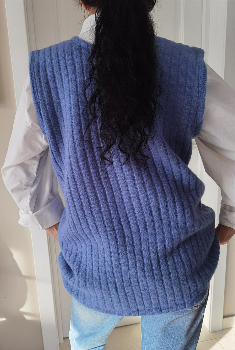 Puede incluir: Un chaleco de punto azul sin mangas con textura de canal&eacute;. El chaleco se lleva sobre una camisa blanca abotonada.