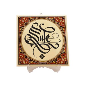 Könnte beinhalten: Eine quadratische Keramikfliese mit einem dekorativen Rand in Rot-, Gold- und Schwarztönen. Die Mitte zeigt ein kreisförmiges Design mit cremefarbenem Hintergrund und schwarzer Kalligraphie, die "Life" lautet.