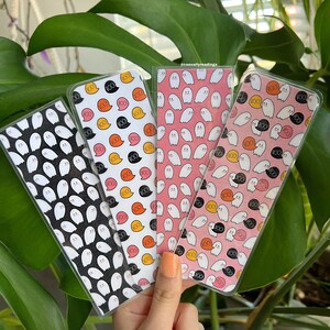 May include: Three ghost-themed bookmarks with different patterns. One bookmark has a black and white ghost pattern, another has a pink and orange ghost pattern, and the third has a white and orange ghost pattern. The bookmarks are all rectangular and have rounded corners.