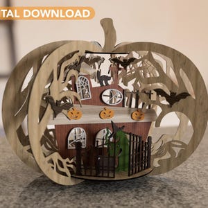 May include: A wooden Halloween pumpkin decoration with a carved haunted house design. The house has a green door, windows, and a roof with bats and a spider web. The pumpkin is surrounded by carved trees and bats.