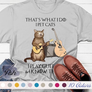 May include: A gray t-shirt with a cat playing a guitar and the text "That's what I do I pet cats I play guitar & I know things" printed on it.