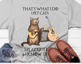 May include: A gray t-shirt with a cat playing a guitar and the text "That's what I do I pet cats I play guitar & I know things" printed on it.