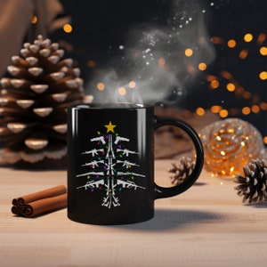 May include: Black coffee mug with a white design of a Christmas tree made of guns with colorful lights. The mug is on a wooden surface with cinnamon sticks and pine cones.