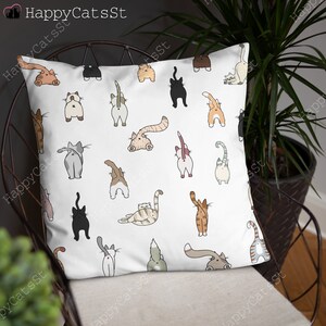 May include: White throw pillow with a repeating pattern of cartoon cats with their tails in the air. The cats are in various colors, including black, white, brown, orange, and gray.