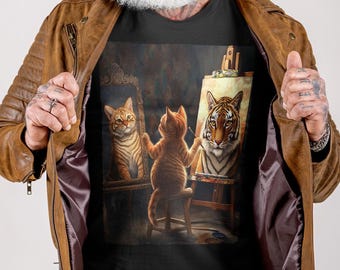 May include: A black t-shirt with a painting of a cat painting a self-portrait as a tiger. The cat is sitting on a stool in front of an easel. The painting is in a realistic style.