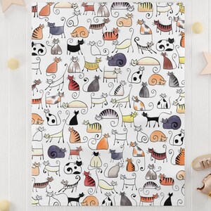 May include: White throw blanket with a repeating pattern of black, gray, orange, and yellow stylized cats. The cats are drawn in a simple, cartoon style.