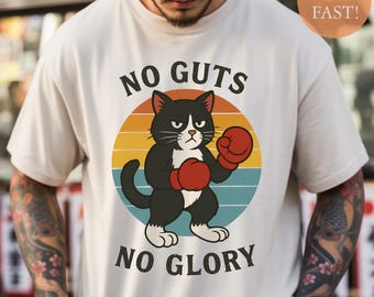 Puede incluir: Camiseta color crema con un gato de dibujos animados con guantes de boxeo rojos, sobre un círculo con colores de atardecer. El texto "NO GUTS NO GLORY" está impreso encima y debajo de la ilustración del gato. Prenda informal.