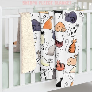 May include: A white sherpa fleece blanket with a colorful cat print. The blanket features a variety of cats in different poses and colors, including orange, black, white, and gray. The blanket is soft and cozy, perfect for snuggling up on the couch or in bed.