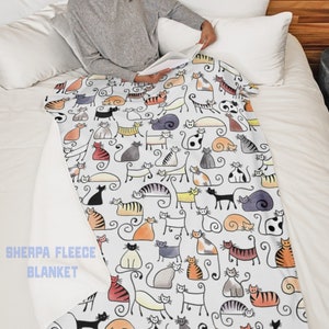 May include: White sherpa fleece blanket with a colorful cat print. The blanket features a repeating pattern of stylized cats in various colors and poses. The text "Sherpa Fleece Blanket" is printed in the bottom left corner.