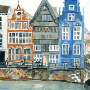 May include: A watercolor painting depicting three multi-story buildings along a canal. The left building is orange, the center is dark gray, and the right is blue. Each structure features multiple windows, gabled roofs, and a stone embankment.