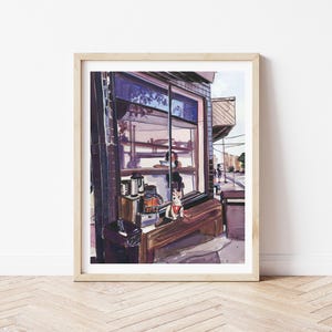 May include: Watercolor painting of a cafe scene. The artwork depicts a storefront with a large window, showcasing interior details like coffee machines and a bench. A dog sits on the bench. The painting is framed in a light wood frame.