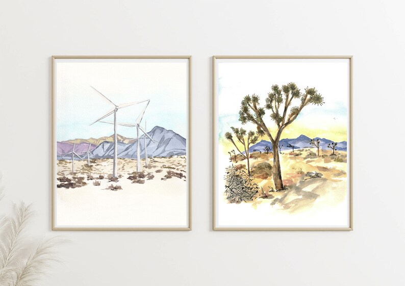 May include: Two framed watercolor paintings. The first painting depicts a desert landscape with wind turbines and mountains in the background. The second painting shows a Joshua Tree in the foreground with a desert landscape in the background.