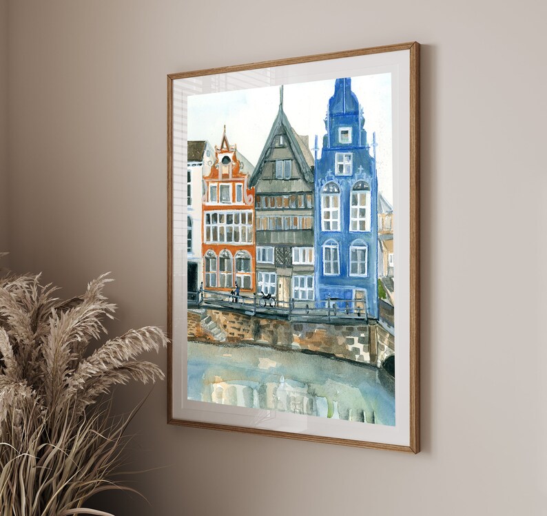 May include: A framed watercolor painting depicting a row of three narrow, multi-story buildings in orange, gray, and blue, situated along a stone embankment above a body of water, with architectural details including multiple windows and gables.