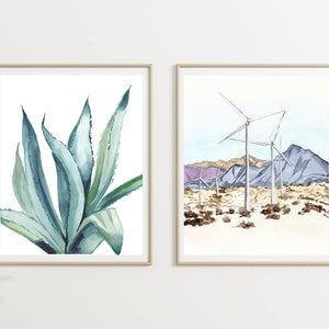 May include: Two framed watercolor paintings. The first painting features a close-up of a blue-green agave plant. The second painting shows a desert landscape with wind turbines and purple mountains.