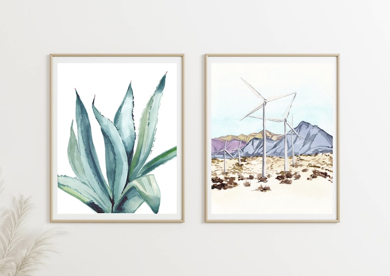 May include: Two framed watercolor paintings. The first painting features a close-up of a blue-green agave plant. The second painting shows a desert landscape with wind turbines and purple mountains.