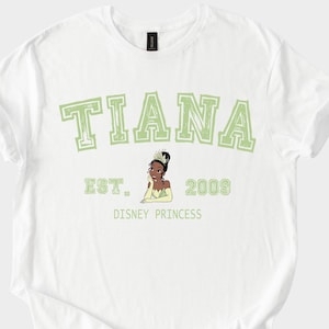 May include: White t-shirt featuring the name "TIANA" in green block letters, with "EST. 2009" and a graphic of a Disney princess. The words "DISNEY PRINCESS" are printed below the graphic.