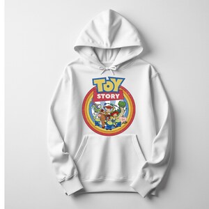 Puede incluir: Sudadera con capucha blanca con un gr&aacute;fico colorido de Toy Story. El dise&ntilde;o presenta el logotipo y los personajes dentro de un marco circular con un borde de arco&iacute;ris. La sudadera tiene un bolsillo delantero y una capucha con cord&oacute;n.