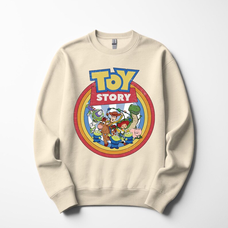 Puede incluir: Sudadera de color crema con un gr&aacute;fico colorido de personajes de la pel&iacute;cula animada "Toy Story". El dise&ntilde;o incluye las palabras "Toy Story" en una fuente azul y amarilla, rodeadas por un c&iacute;rculo de arco&iacute;ris.