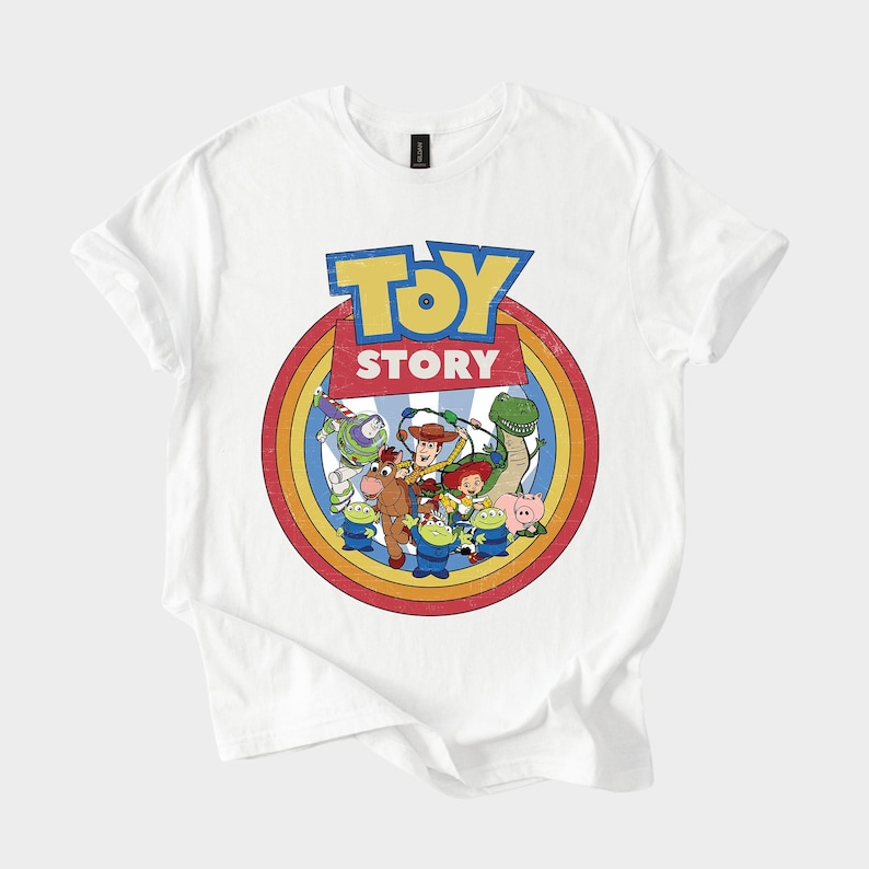 Puede incluir: Camiseta blanca con un dise&ntilde;o gr&aacute;fico colorido de los personajes de la pel&iacute;cula "Toy Story". El dise&ntilde;o incluye el logotipo de la pel&iacute;cula en azul y amarillo, rodeado por un c&iacute;rculo de colores del arco&iacute;ris e ilustraciones de personajes.