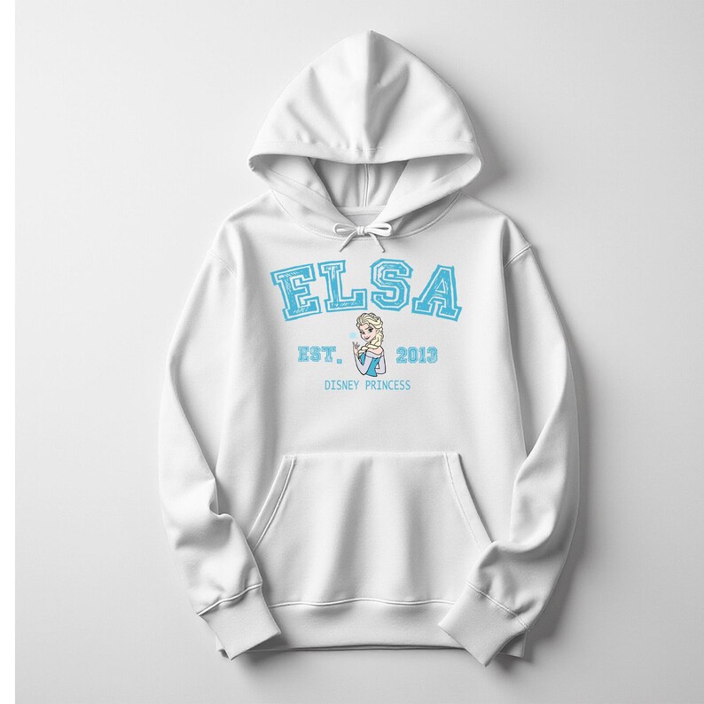 K&ouml;nnte beinhalten: Wei&szlig;er Kapuzenpullover mit dem Namen "ELSA" in hellblauen Blockbuchstaben. Darunter stehen die Worte "EST. 2013" und eine Grafik von Elsa, darunter "DISNEY PRINCESS". Der Pullover hat eine Vordertasche.