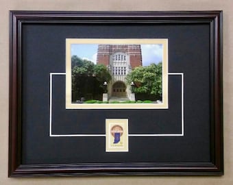 May include: A framed photograph of a brick building with a gold mat and a small gold and blue emblem in the lower right corner.