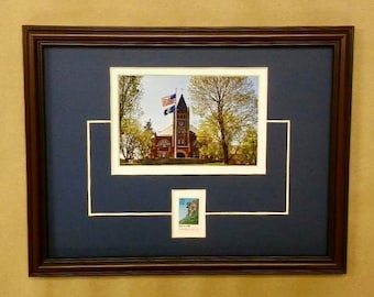 May include: A framed photograph of a brick building with a flagpole and a flag. The building is surrounded by trees. The photograph is matted in white and navy blue with a smaller photograph of a building in the lower right corner.