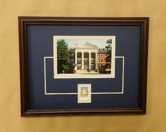 May include: A framed photograph of a brick building with white columns and a white roof. The building is surrounded by trees and grass. A smaller photograph of a sailboat is in the lower right corner of the frame.