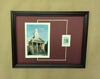 May include: A framed photograph of a white building with a steeple, surrounded by a maroon mat and a white mat. A smaller framed photograph of a building is in the upper right corner.